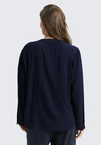 Blouse bleu marine à manches longues avec une coupe décontractée, dotée d'un empiècement froncé et de poignets boutonnés, fabriquée dans un tissu léger et texturé.