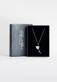 Sølvblomstvedhæng på en delikat kæde, vist i en mørk boks med et tekstureret sølvfælde, der bærer 'Sofia Milani Jewels' logo.