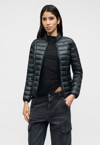 Μαύρο μπουφάν τύπου puffer με φερμουάρ μπροστά, γιακά που στέκεται, σχεδιασμό με ραφές και λεία υφή, συνοδευόμενο από χαλαρό σκουρόχρωμο παντελόνι cargo.