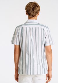 Camicia a maniche corte bianca con righe verticali blu-verdi, dotata di colletto a risvolto e vestibilità comoda. Il retro presenta un dettaglio con piega centrale.