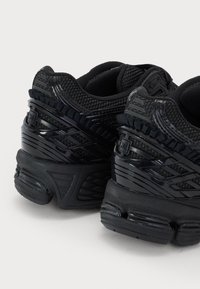 Black athletic shoes with a textured mesh upper, shiny plastic accents, and a thick rubber sole featuring unique grip patterns.