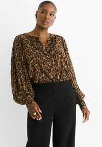 Brown and black leopard print blouse with a buttoned neckline, long puff sleeves, and light, flowing fabric, paired with black pants.