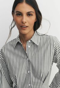 Striped button-up shirt in gray and white, featuring a collar and long sleeves. Made of textured fabric with visible buttons.