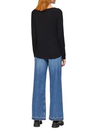 Schwarzes Langarmshirt kombiniert mit weiten blauen Jeans aus Denim. Die Jeans haben einen fransigen Saum und dezente Waschdetails. Schwarze klobige Schuhe.