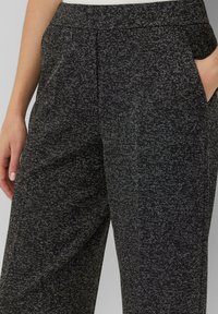 Zwarte broek met een textuurpatroon en witte spikkels, een aansluitende tailleband en zijzakken.