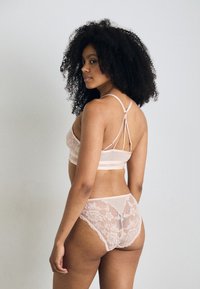 Ensemble de lingerie en rose doux, comprenant un soutien-gorge en tissu transparent avec des accents en dentelle et un dos à bretelles, associé à une culotte assortie bordée de dentelle.