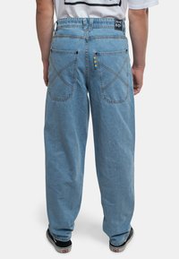 Los jeans de mezclilla azul claro tienen un ajuste holgado con bolsillos traseros de doble costura distintivos y una etiqueta multicolor en la cinturilla.