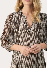 Patterned blouse featuring a chevron design in brown, black, and white. It has a v-neckline and gathered sleeves. Lightweight fabric.