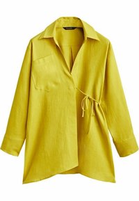 Keltainen pellavapaita, jossa on kaulus, pitkät hihat, etutasku ja solmdetalji vyötäröllä. Ominaisuuksina on löysä, epäsymmetrinen leikkaus.