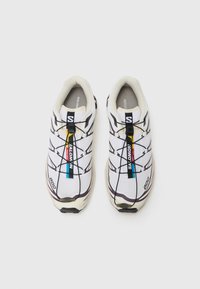 Scarpe da corsa bianche con una tomaia in rete, dettagli neri e viola, sistema di allacciatura elastico e suola in gomma texturizzata.