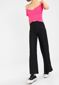 Top rosa con hombros al aire y diseño ajustado, combinado con pantalones de pierna ancha a rayas negras, complementado con zapatillas negras.