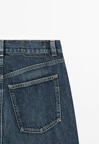 Mörkblå denimjeans med hög midja, en bakficka och kontrastsömmar längs sömmarna. Slät textur.