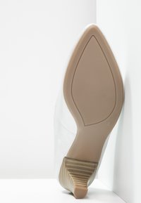 Chaussures blanches avec un bout pointu, une tige texturée et un talon bas effilé. Caractérisées par une semelle beige lisse avec de subtiles rayures horizontales.