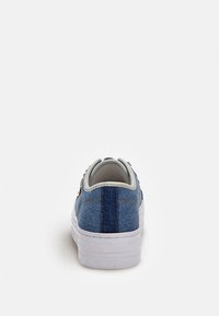 Baskets en denim avec une tige bleue, une semelle blanche et des accents gris. Comprend une couture arrière proéminente et un détail de quincaillerie métallique.