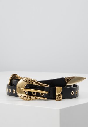 Ceinture en cuir noir avec boucle dorée texturée, œillets et pointe effilée, enroulée sur une surface blanche sur fond gris clair uni.