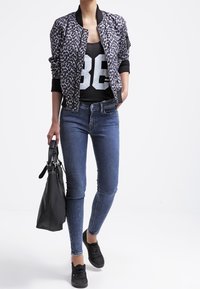 Chaqueta bomber de estampado de leopardo, top negro con el número blanco "86", vaqueros ajustados azules, bolso negro, zapatillas negras. Conjunto urbano casual.