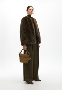 Brown faux fur jacket, green turtleneck, olive wide-leg trousers. Holds a textured brown handbag with a braided handle and gold hardware.