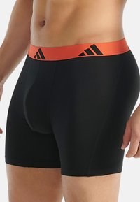 Svarta boxershorts i stretchigt material, med en bred orange midja som har svarta logodetaljer, designade för komfort och stöd.