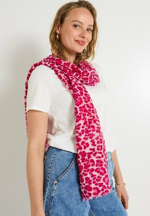 Bufanda rosa con estampado de leopardo, textura suave y bordes con flecos, colocada sobre el cuello encima de una camiseta blanca y unos jeans de mezclilla.