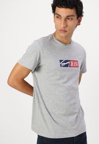 Pilkas medvilninis T-palaidinukas su apvalia iškirpte, viduryje su mėlynu, raudonu ir baltu "Tommy Jeans" logotipu. Trumpi rankoviai, laisvas pritaikymas.