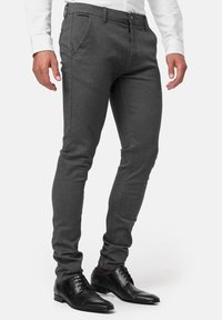 Pantalon gris cintré en tissu texturé, doté d'une braguette zippée, de poches latérales et de passants pour ceinture, associé à des chaussures habillées noires.