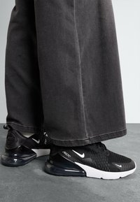 Sneakers Nike Air Max 270 neri con tomaia texturizzata, suola con cuscino d'aria visibile e accenti bianchi. Indossati con pantaloni larghi e scuri.