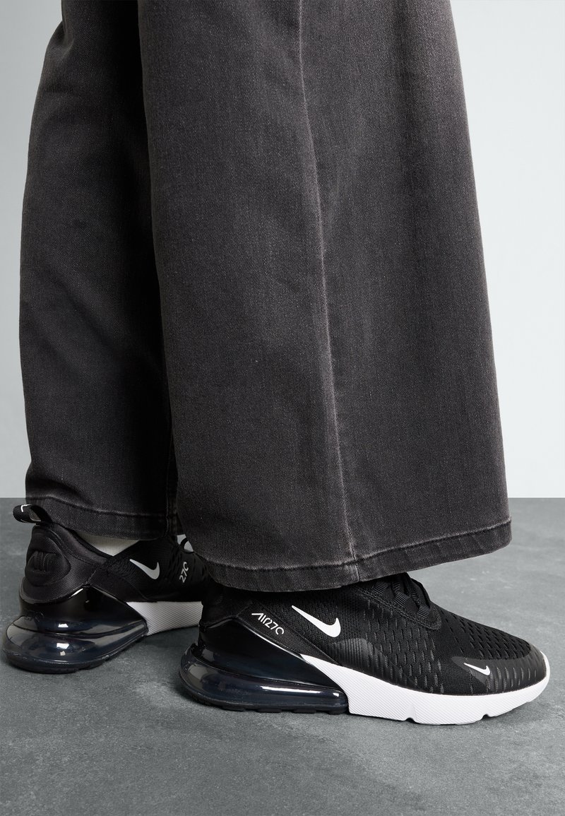 Sneakers Nike Air Max 270 neri con tomaia texturizzata, suola con cuscino d'aria visibile e accenti bianchi. Indossati con pantaloni larghi e scuri.