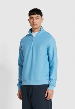Lichtblauwe pullover met rits in een gebreide textuur. Heeft een ontspannen pasvorm, geribde manchetten en een klein logo op de borst.