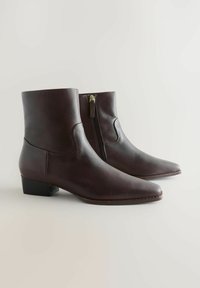 Pair of dark brown leather ankle boots with low heels and side zippers, shown on a neutral background.