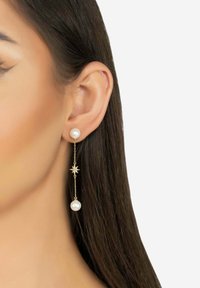 Gold drop earrings featuring white pearls, star accents, and a chain design, showcased next to an ear, highlighting their elegance.
