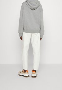 Gray hooded sweatshirt with ribbed cuffs paired with white loose-fitting pants. Features beige and orange sneakers with a chunky sole.