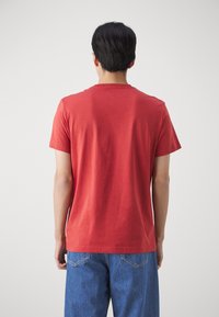 Rød bomuld T-shirt med korte ærmer og rund halsudskæring, båret med blå jeans. Simpel design, blød tekstur og ingen synlige mønstre.