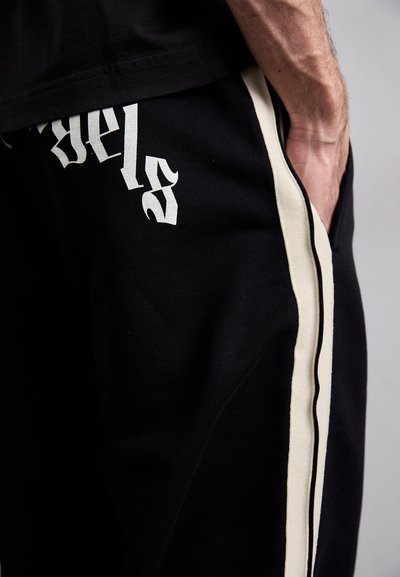 Zwarte sweatpants met een wit bedrukt ontwerp, voorzien van een gestructureerde stof, contrasterende crèmekleurige zijstrepen en een ontspannen pasvorm.