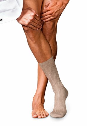 Beige kniekous met geribbelde textuur gedeeltelijk op een voet, in contrast met een blote voet. Gladde huidkleur zichtbaar, wat de details van de kous accentueert.