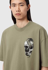 Olivengrøn T-shirt med et stort motiv af en kranium, hvor en slange er viklet om, detaljeret med blomster og skygger.