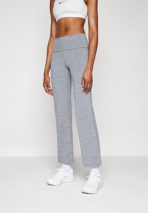 Strakke grijze sportbroek gedragen met witte sneakers en een wit cropped Nike sport-bh bij een staand persoon.