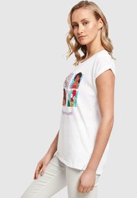 Hvid bomuld t-shirt med et farverigt grafisk design med animerede figurer og ordet "Teamwork" trykt i lilla. Korte ærmer.