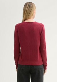 Maroon knit sweater with long sleeves, crew neckline, ribbed hem, and seamless shoulder design. Soft texture, fitted silhouette.