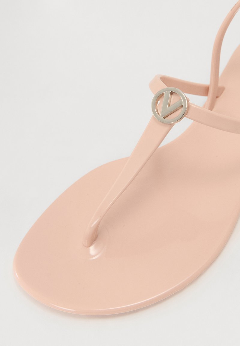 Tongs en caoutchouc rose avec une bride entre les orteils, texture lisse et un accent en logo circulaire argenté sur la bride.