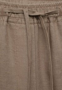 Pantalons en lin à cordon de serrage dans une couleur marron atténuée, avec une taille élastique et un nœud à l'avant. Le tissu présente un tissage texturé.