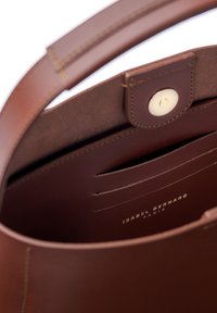Brown leather handbag interior with a button closure, card slots, and smooth texture. "ISABEL BERNARD" embossed inside.