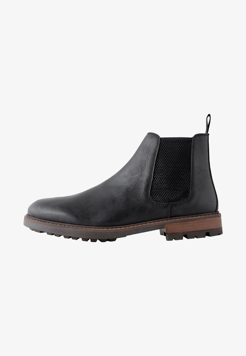 Bottine Chelsea en cuir noir avec panneau latéral élastique texturé, languette au talon, semelle marron et semelle extérieure à crampons robustes.