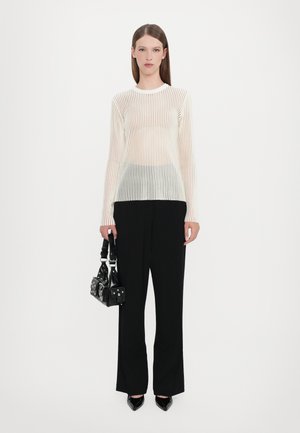 Bluză albă cu mâneci lungi și dungi verticale, fabricată dintr-un material transparent. De asemenea, sunt incluse pantaloni negri largi și o geantă mică neagră cu cuie.