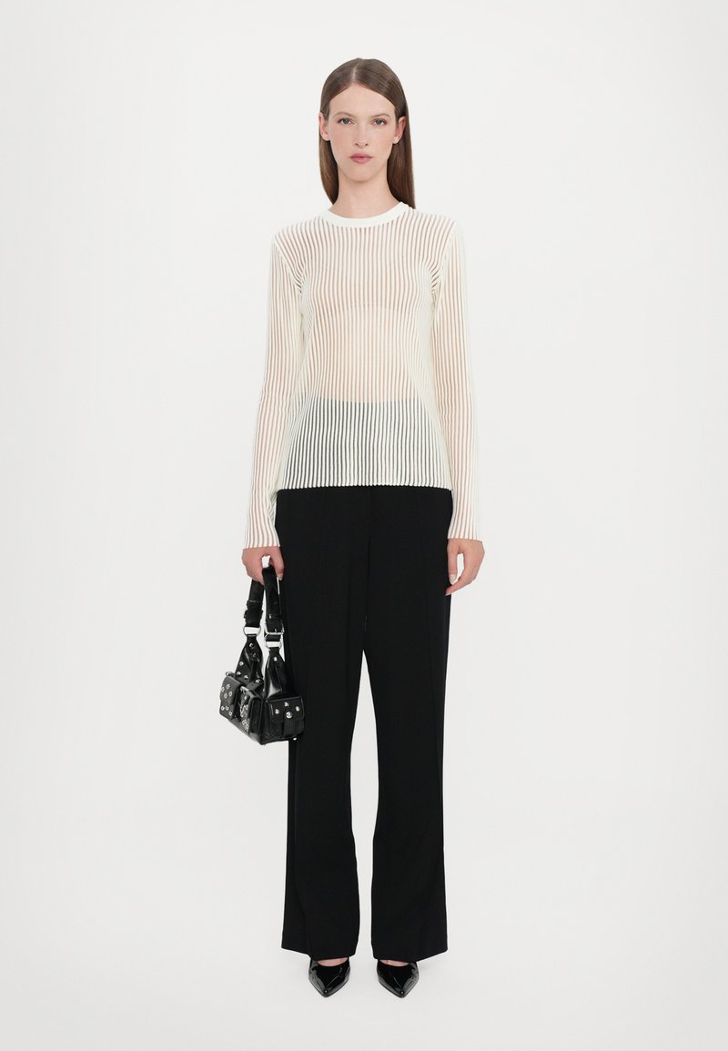 White long-sleeve top with vertical stripes, made of sheer fabric. Black wide pants and a small black bag with studs are also featured.