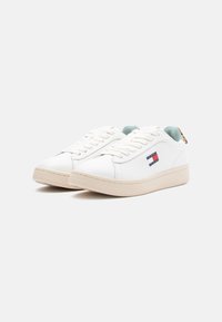 Λευκά δερμάτινα sneakers με μπεζ καουτσούκ σόλες, που διαθέτουν σχέδιο με κορδόνια, μπλε λεπτομέρειες στο εσωτερικό και ένα μικρό λογότυπο στο πλάι.