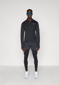 Nike sportoutfit bestående av en långärmad svart tröja, mörka shorts, svarta leggings och vita sneakers. Anmärkningsvärda blå solglasögon fulländar stilen.