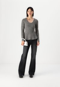 Grå strikkegenser med scoop-utsnitt og flagrende hem, parret med mørke flagrende jeans. Modellen holder en liten hvit håndveske.