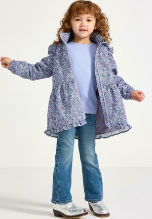 Jasnofioletowa kurtka w kwiatowy wzór z falbanami na ramionach, zamkiem błyskawicznym i marszczonym pasem. W zestawieniu z jasnoniebieską bluzką i rozkloszowanymi jeansami.