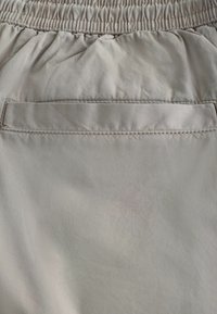 Beżowe spodnie z elastycznym pasem i poziomą tylną kieszenią z klapką zapinaną na szew.