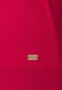 Fuchsia stickad tröja med ribbad nederkant och en gyllene logotagg med "1960"-detalj. Slät textur med tätstickad design.